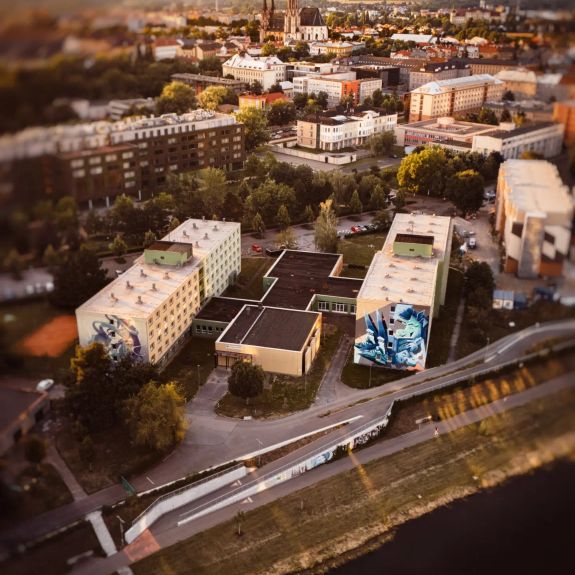 Bývalý U-klub = budoucí U-klub! 🔜

„Učko“ – tak se po téměř 3 dekády říkalo legendárnímu studentskému klubu na naší koleji Generála Svobody. Od 80. let minulého století fungoval jako jedno z center olomouckého kulturního dění. Za sametové revoluce tu vystoupil (a svůj podpis na zdi zanechal) Karel Kryl. Na jeho pódiu se vystřídaly stovky českých i zahraničních hudebníků a kapel a stal se místem setkávání několika generací studentů i olomoucké veřejnosti. V roce 2018 se ale jeho dveře pomyslně zavřely – klub přestal sloužit svému původnímu účelu a jeho prostor se přechodně využíval jako skladovací prostor či tělocvična.

Teď se ovšem blíží jeho návrat v novém. Vedení UP dnes veřejně představilo projekt rekonstrukce, která U-klub vrátí zpět na kulturní mapu Olomouce.

Návrh vzniklý ve spolupráci s kreativním studiem @mimokolektiv počítá se zachováním původní dispozice a respektováním charakteru místa. Zároveň ale vytvoří flexibilní víceúčelový sál s mobilním vybavením a moderním technickým zázemím. Vznikne nová terasa propojená s areálem kolejí a fasáda bude nově otevřena směrem do univerzitního kampusu a k řece Moravě.

Nový U-klub nebude pouhým koncertním sálem. Bude otevřeným komunitním centrem pro studentskou kulturu, divadelní představení, debaty, workshopy, filmové projekce, činnost studentských spolků i další univerzitní akce. Tak, aby nabídl prostor pro studentskou iniciativu a kreativitu a stal se jedním z přirozených center univerzitního života.

Koukněte na vizualizace a těšte se – už příští akademický rok v letním semestru!

#univerzitnimesto